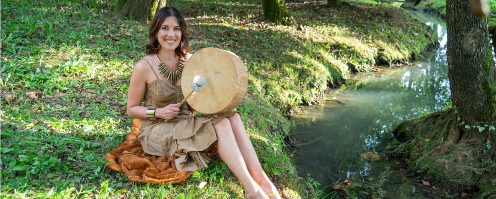 Psicologa online Transpersonale che suona il tamburo seduta in mezzo alla natura incontaminata